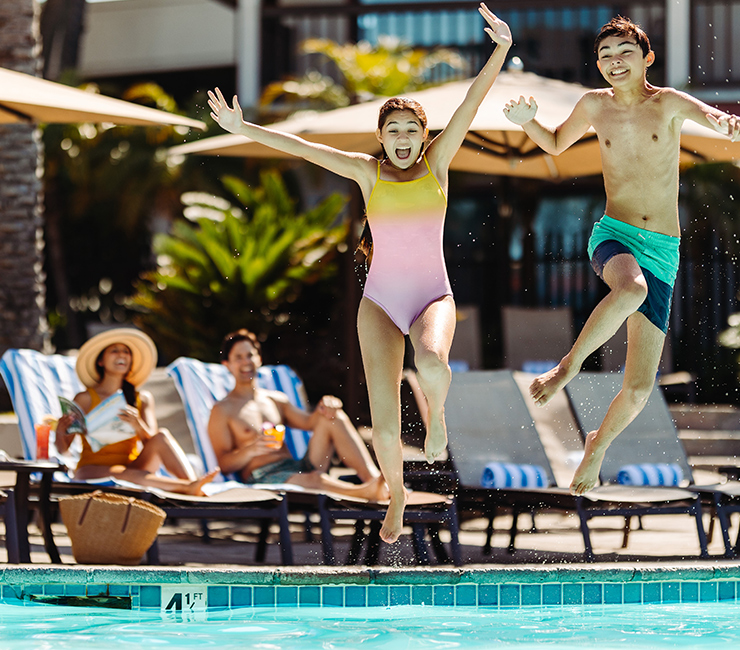 Kids jumping into pool with parents watching in background